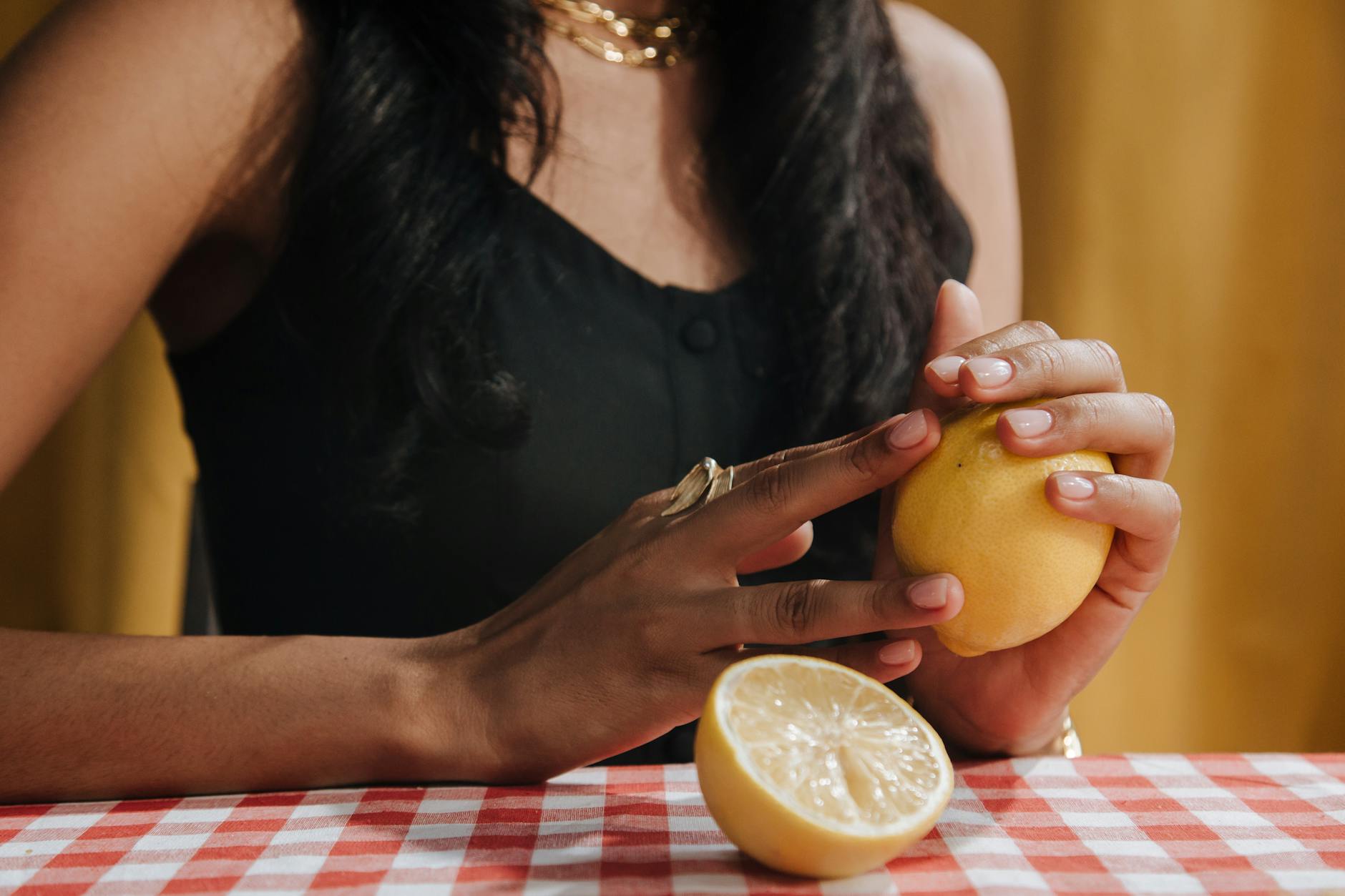 Hand holding a fresh lemon on soft pink background surrounded by additional lemons