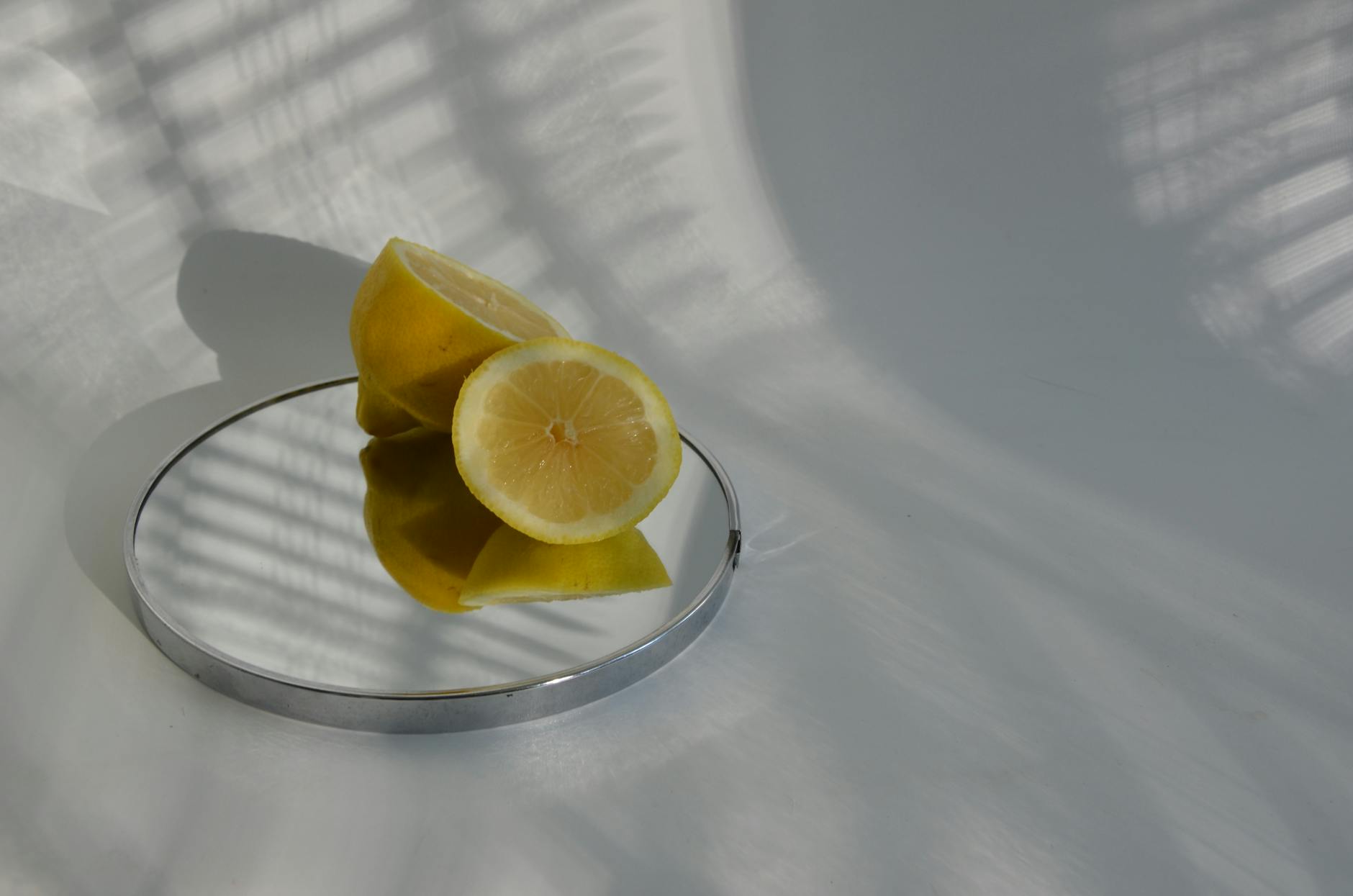 A hand with white nails holding a fresh lemon on soft pink background surrounded by additional lemons
