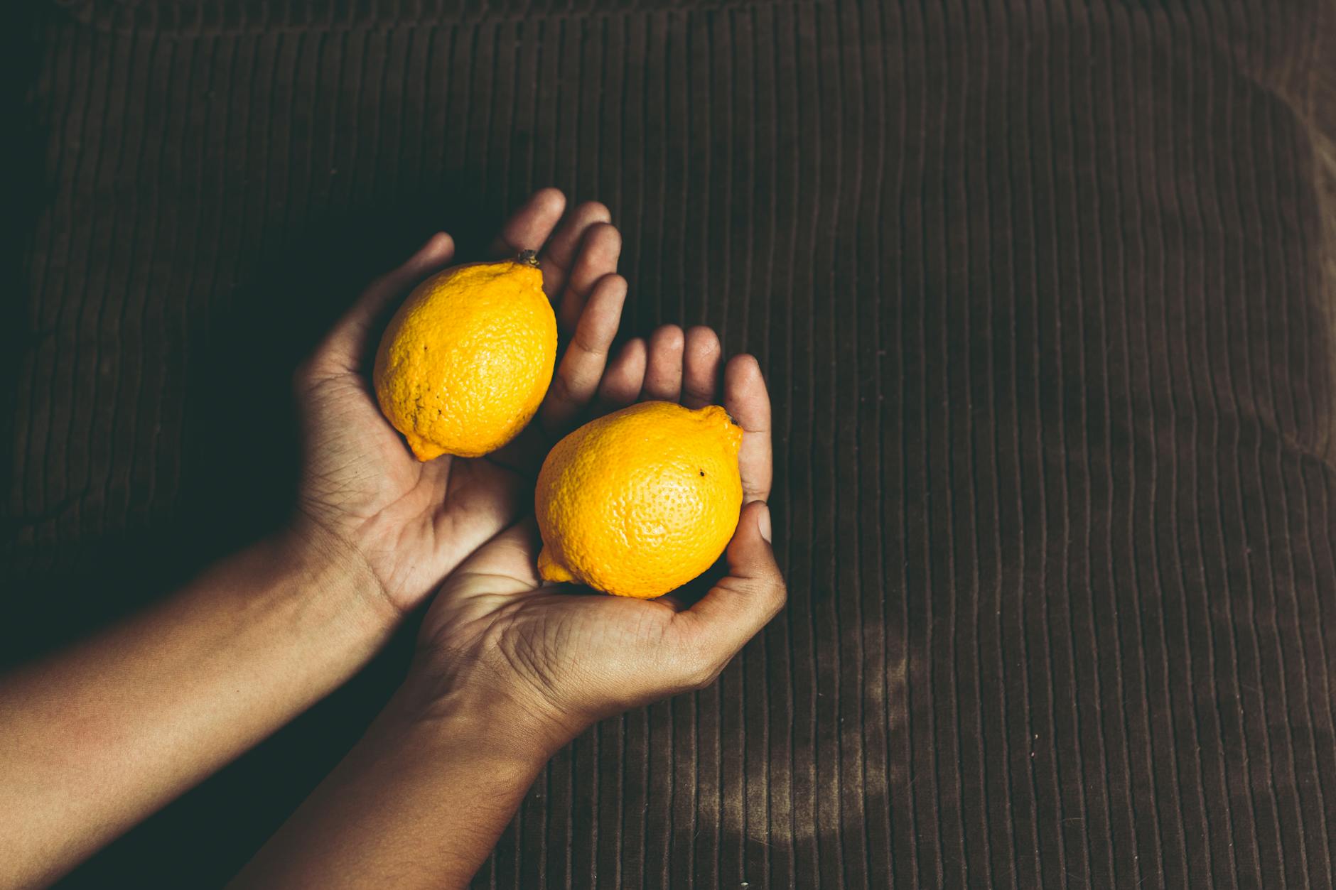 Close-up of two fresh lemons held in cupped hands on a brown surface, symbolizing freshness and renewal.