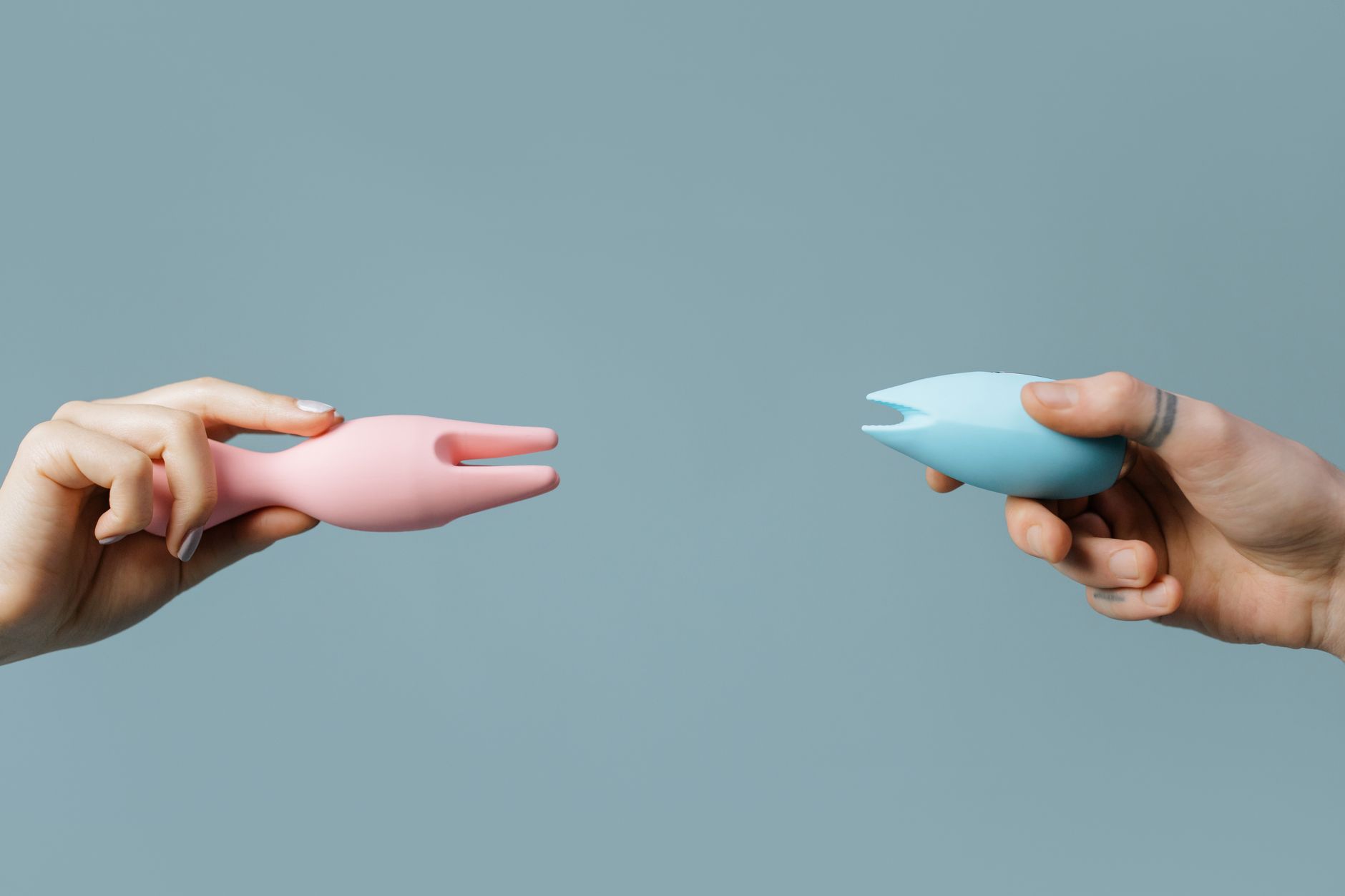Two hands holding colorful silicone vibrators against a pastel background, representing choice and confidence.