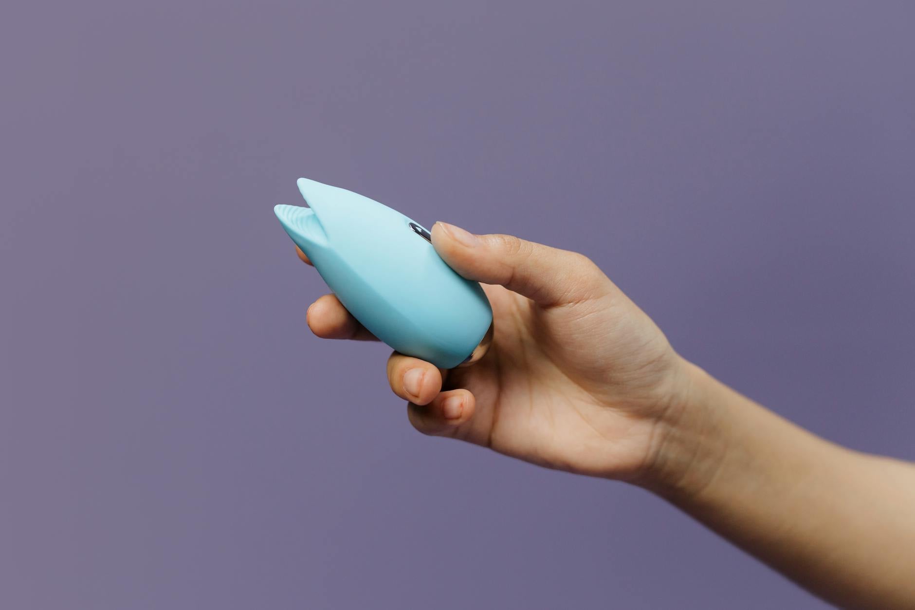 A blue silicone lemon clitoral vibrator held in hand against a solid purple background, symbolizing modern pleasure and self-care.