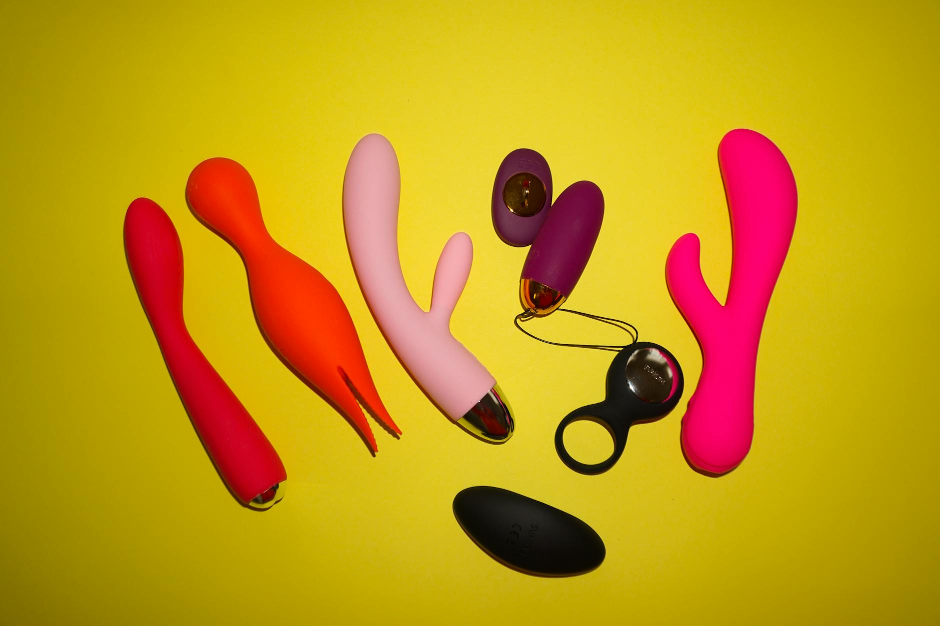 Colorful arrangement of adult sex toys displayed on a bright yellow background